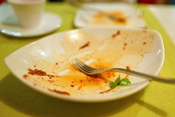 Empty and dirty plate with a fork and bits of food after lunch on the table
