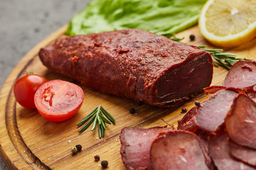 Armenian basturma or Pastirma on wooden cutting board decorated with spices, lettuce, lemon and tomatoes. Meat smoked jerky good as Beer snack