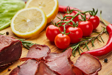 Armenian basturma or Pastirma on wooden cutting board decorated with spices, lettuce, lemon and tomatoes. Meat smoked jerky good as Beer snack