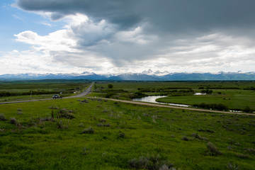A view of the Teton mountains from several miles north of Victor, Idaho, with green agricultural fields and interesting clouds overhead