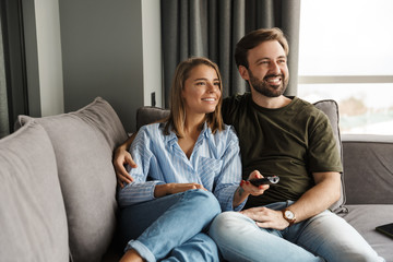Photo of joyful couple watching TV and using remote control