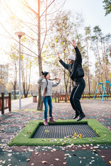 Mom and her daughter jumping together on trampoline in autumn park