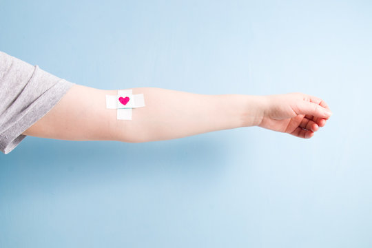 female hand with a band-aid glued with a cross on a vein, heart on a band-aid, blood donor concept, blue background, copy space