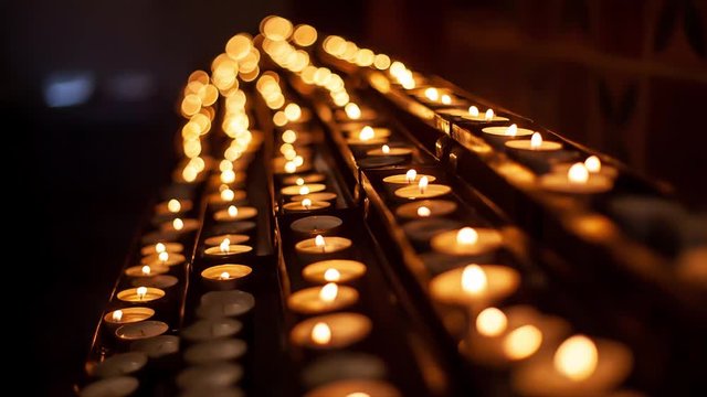 Rows of hundreds burning votive candles in dark moody sacral environment, background texture, shallow depth of focus, light bokeh effect. Memory and prayer, contemplation, church small candles concept