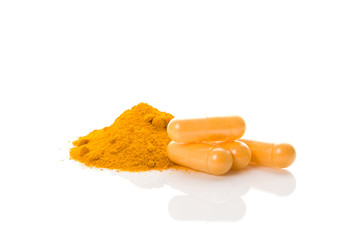 Turmeric powder and yellow capsules on white background.