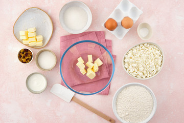 flour, cottage cheese in bowl and milk, eggs. products for making cheesecakes on a pink backround.