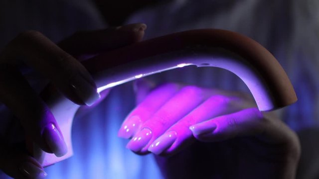 woman using an ultraviolet lamp for fixing gel nail polish at home. Gel shellac nails painting and fixing.
