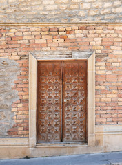 dilapidated red brick wall and old brown carved wooden front door (closed), no people