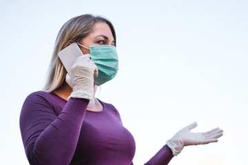 Young person talking with mobile phone outdoor wearing face mask and gloves for Covid-19 virus prevention - Girl speaking with smartphone outside during quarantine isolation - Focus on hand glove
