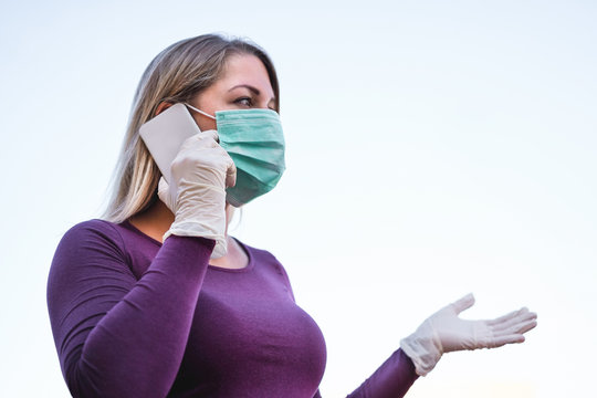 Young person talking with mobile phone outdoor wearing face mask and gloves for Covid-19 virus prevention - Girl speaking with smartphone outside during quarantine isolation - Focus on hand glove