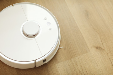 white robot vacuum cleaner cleans the floor from debris,home cleaning with an electric vacuum cleaner,vacuum cleaner electric robot cleaning technology,top view of a robot vacuum cleaner.