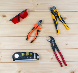 Set of tools for repai and carpentry. Red protective glasses, flat-nose pliers, adjustable spanner, key, roulette and level. Top view of carpenter's tools on wooden background. Construction industry.