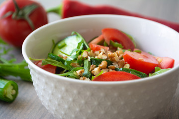 Healthy fresh summer salad with cucumbers, tomatoes, fresh arugula, chopped walnuts, pepper, olive oil and lemon juice on a rustic wooden surface