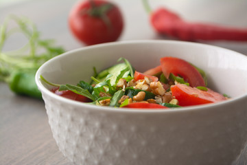 Healthy fresh summer salad with cucumbers, tomatoes, fresh arugula, chopped walnuts, pepper, olive oil and lemon juice on a rustic wooden surface