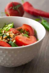 Healthy fresh summer salad with cucumbers, tomatoes, fresh arugula, chopped walnuts, pepper, olive oil and lemon juice on a rustic wooden surface