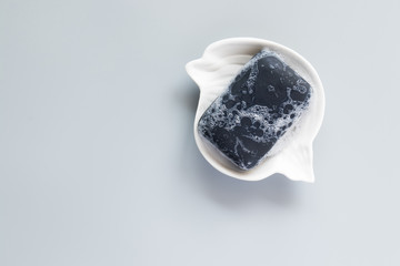 Black soap bar and foam in the soap dish on a grey background. Hand made soap. For protect, health.