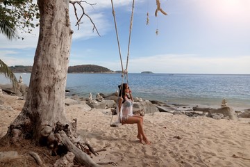     young attractive sexy woman on vacation sitting on a swing by the sea, tropical beach      
