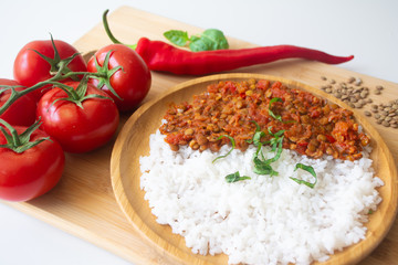Red lentil ragu dahl with tomatoes, pepper, greens and rice on a wooden plate