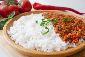 Red lentil ragu dahl with tomatoes, pepper, greens and rice on a wooden plate