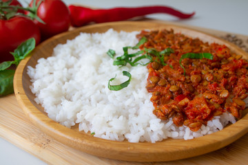 Red lentil ragu dahl with tomatoes, pepper, greens and rice on a wooden plate