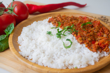 Red lentil ragu dahl with tomatoes, pepper, greens and rice on a wooden plate