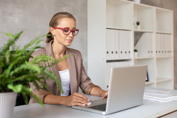 Blond woman in glasses working with lapatop. Office worker