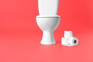 Toilet bowl with rolls of paper on color background