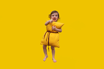 a beautiful little girl embracing a big yellow orthopedic and healthy pillow, showing her hand class and smiling in a bright yellow background - the pillow concept for a healthy sleep