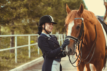 Beautiful professional female jockey standing near horse. woman horse rider is preparing to...