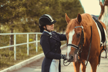 horsewoman jockey in uniform standing with black horse outdoors