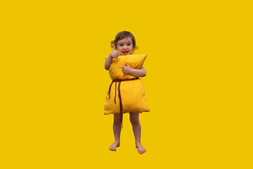 a beautiful little girl embracing a big yellow orthopedic and healthy pillow, showing her hand class and smiling in a bright yellow background - the pillow concept for a healthy sleep