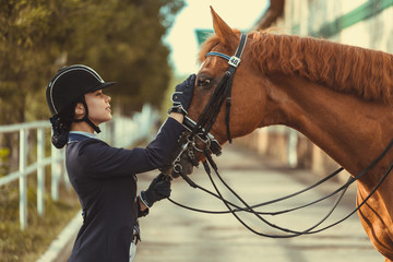 horsewoman jockey in uniform standing with black horse outdoors
