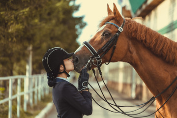 Young teenage girl equestrian kissing her favorite red horse. Multicolored outdoors horizontal image. Dressage outfit  - 344501037
