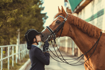 Young teenage girl equestrian kissing her favorite red horse. Multicolored outdoors horizontal...