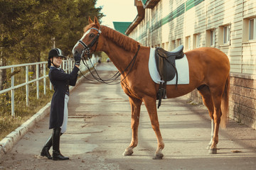 Beautiful professional female jockey standing near horse. woman horse rider is preparing to...