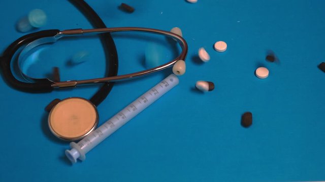 Multi-colored pills fall on a blue background. On a blue background gloomy injection, pills and statoscope. The concept of medicine and drug addiction.