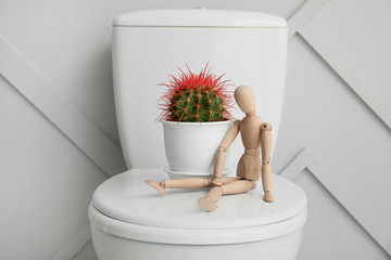 Toilet bowl, cactus and wooden human figure in restroom. Hemorrhoids concept