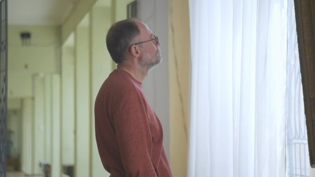 The man in the gallery standing at the window considering artwork.