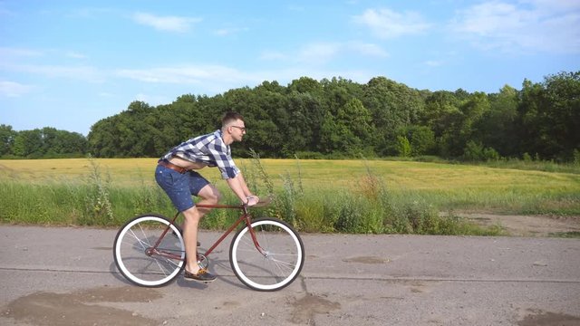 Young handsome man riding at vintage bicycle in the country road. Sporty guy cycling at the track. Male cyclist riding fixed gear bike at highway. Healthy active lifestyle Close up