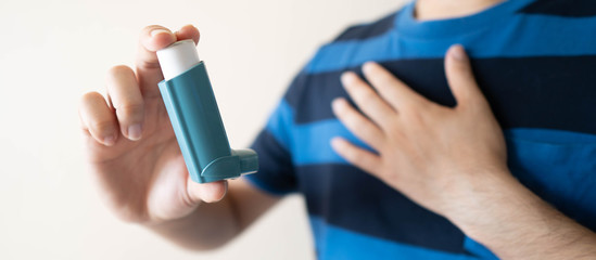 Young man using blue asthma inhaler for relief asthma attack. Pharmaceutical product is used to prevent and treat wheezing and shortness of breath caused asthma or COPD. Health care concept. Close up. - obrazy, fototapety, plakaty