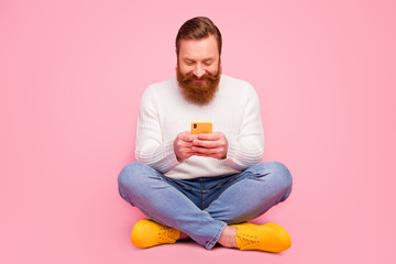 Full size photo positive cheerful guy hipster sit floor legs crossed use smart phone typing social network comment wear denim trendy style jeans white jumper isolated pastel color background