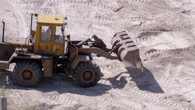 An Old Bulldozer Moves Sand Using a Bucket on Construction Site