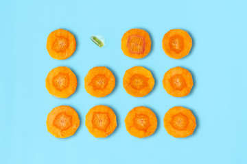 Sliced carrot pattern with capsule on pastel blue background. Fish oil pills. Medicine healthcare...