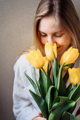 Beautiful young blond woman with tulip bouquet. Close-up spring portrait. Happy and romantic woman at home interior with sun rays and a bouquet of yellow flowers. Girl in underwear and white shirt