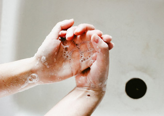 Fototapeta premium Washing hands with soap. Young woman washing hands with soap over sink in bathroom, closeup. Covid 19. Coronavirus. Hygiene. Cleaning Hands.
