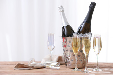 Bucket with bottles and glasses of champagne on table