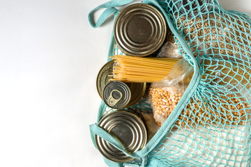 Canned meat and fish, spaghetti paste, sugar, dry peas and pearl barley in bundles in a blue mesh bag on a white background
