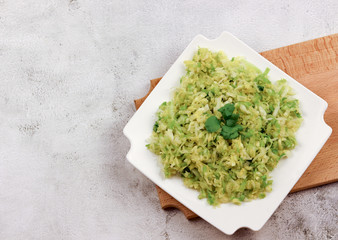 Green cabbage salad on a rectangular plate on a light gray background. Top view, flat lay