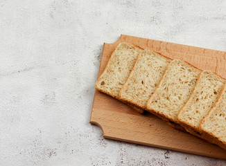 Slices of multigrain bread on a wooden cutting board on a light gray background. Top view, flat lay