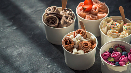 Rolled ice cream in cone cups on dark background. Different iced rolls or Thai style rolled ice cream with copy space for text or design. Banner. Natural hard daylight